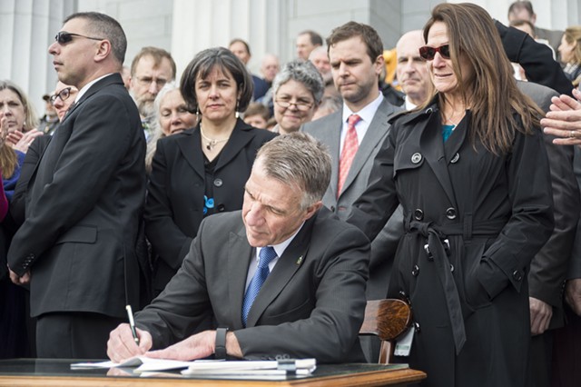 Governor Phil Scott signing gun control bills in 2018 amid a mix of applause and jeers - JOSH KUCKENS