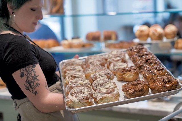 Sara Casper holding a tray of maple-pecan sticky buns and cinnamon rolls with cream cheese frosting - DARIA BISHOP