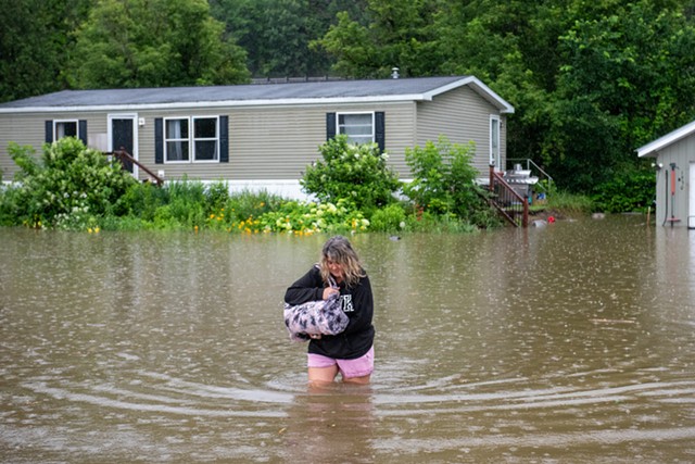 A woman wading through rising floodwaters to leave a home on Route 2 in Waterbury - KEVIN GODDARD