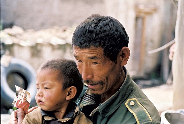 A Tibetan man with his son, holding a picture of the Dalai Lama - COURTESY