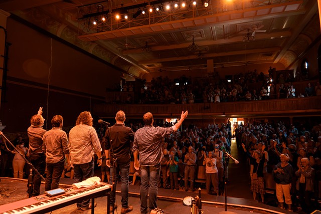 Actors on stage gesture to a crowd giving them a standing ovation