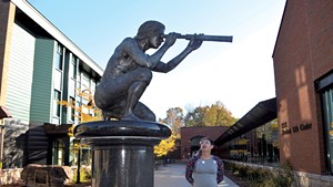 Jayy Covert standing next to the sculpture of Samuel de Champlain at Champlain College