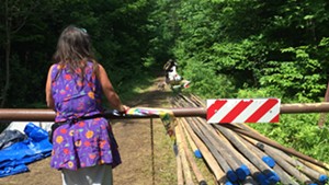 A woman who goes by “Feather” stands at the campsite entrance by poles that will be used to construct teepees.