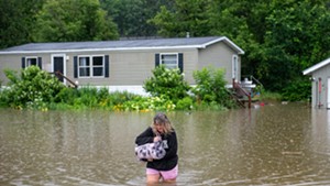 A woman wading through rising floodwaters to leave a home on Route 2 in Waterbury