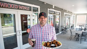 Collin Sourdiff holding a plate of Wicked Wings and a Woodstock Inn & Brewery brown ale