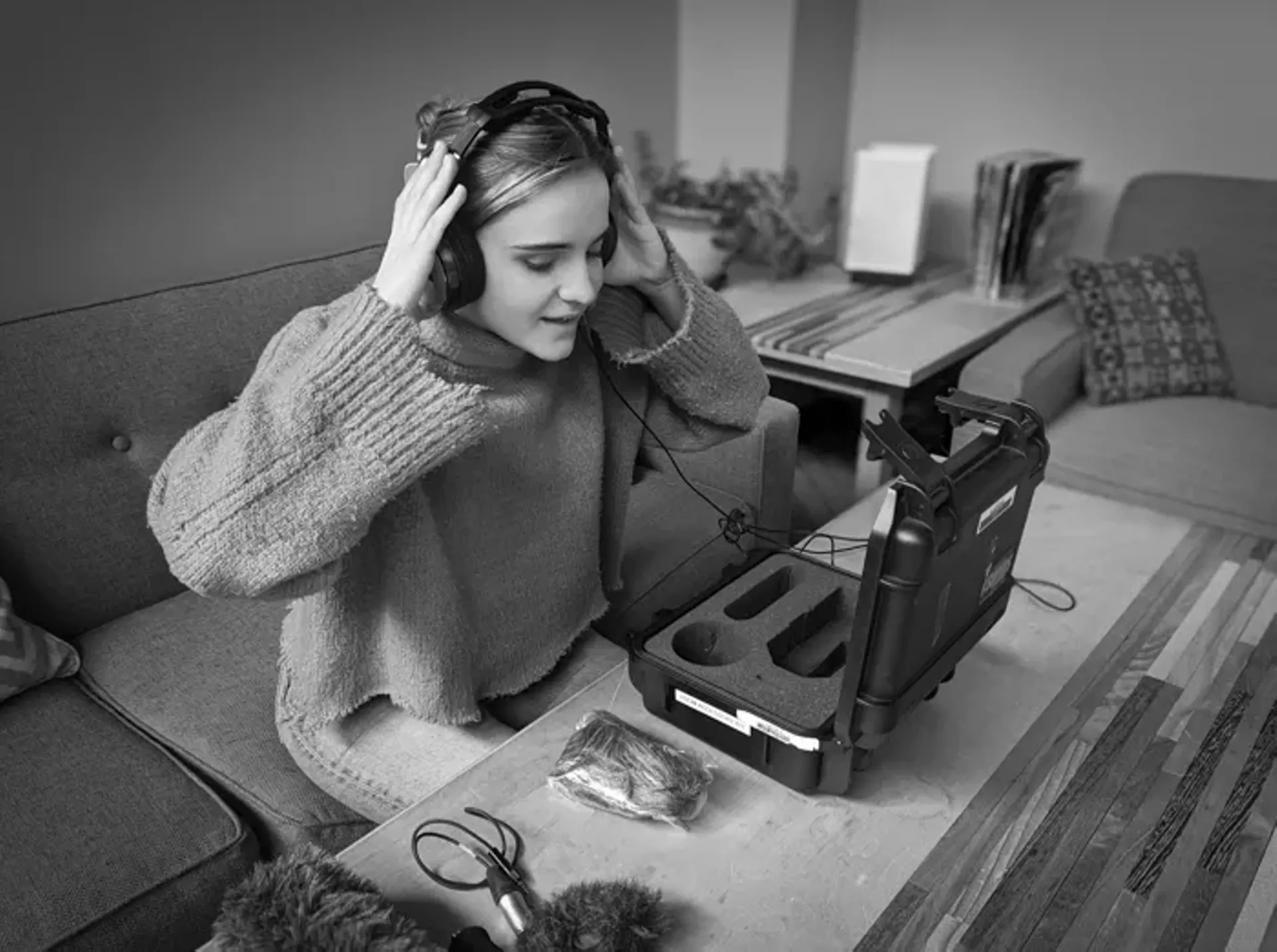A person wearing headphones and looking at audio equipment on a table